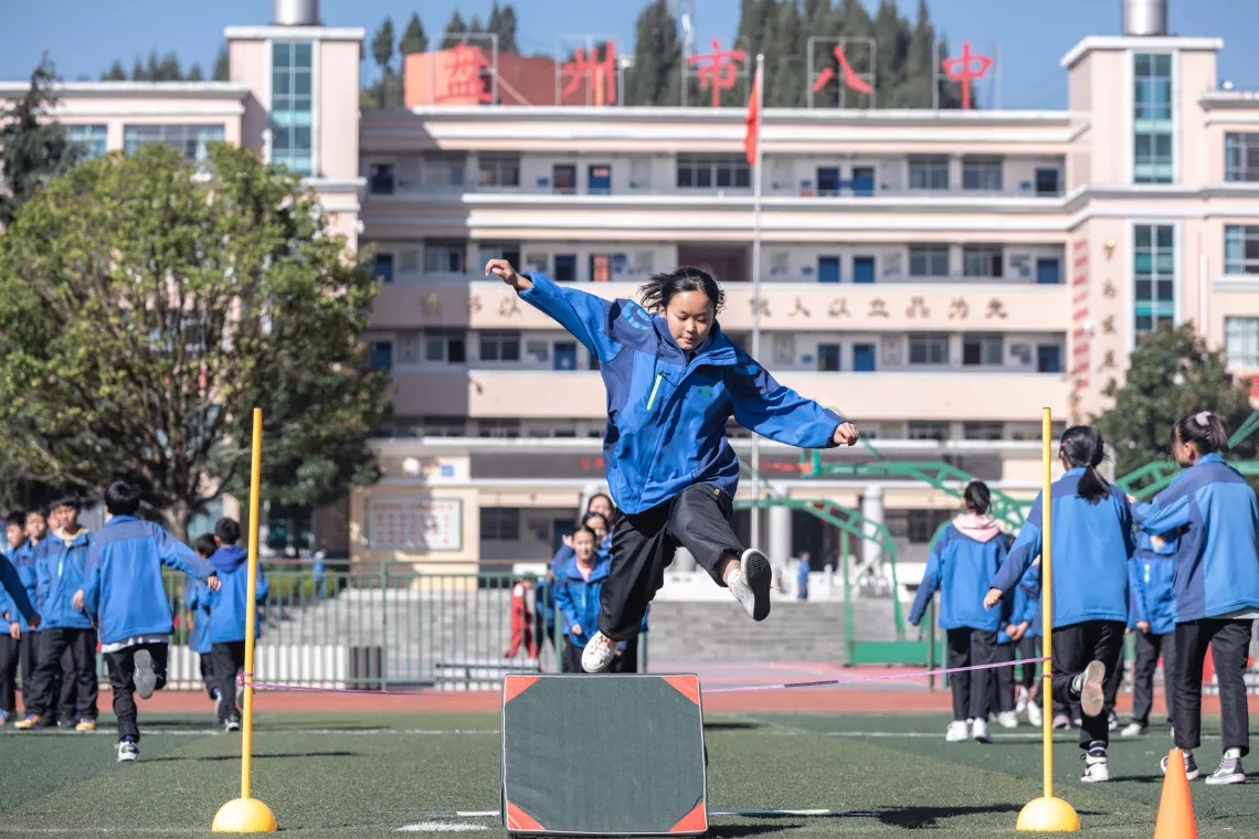 A girl jumps over a barrier during a PE class at a middle school in Panzhou, Guizhou Province, in November 2020.