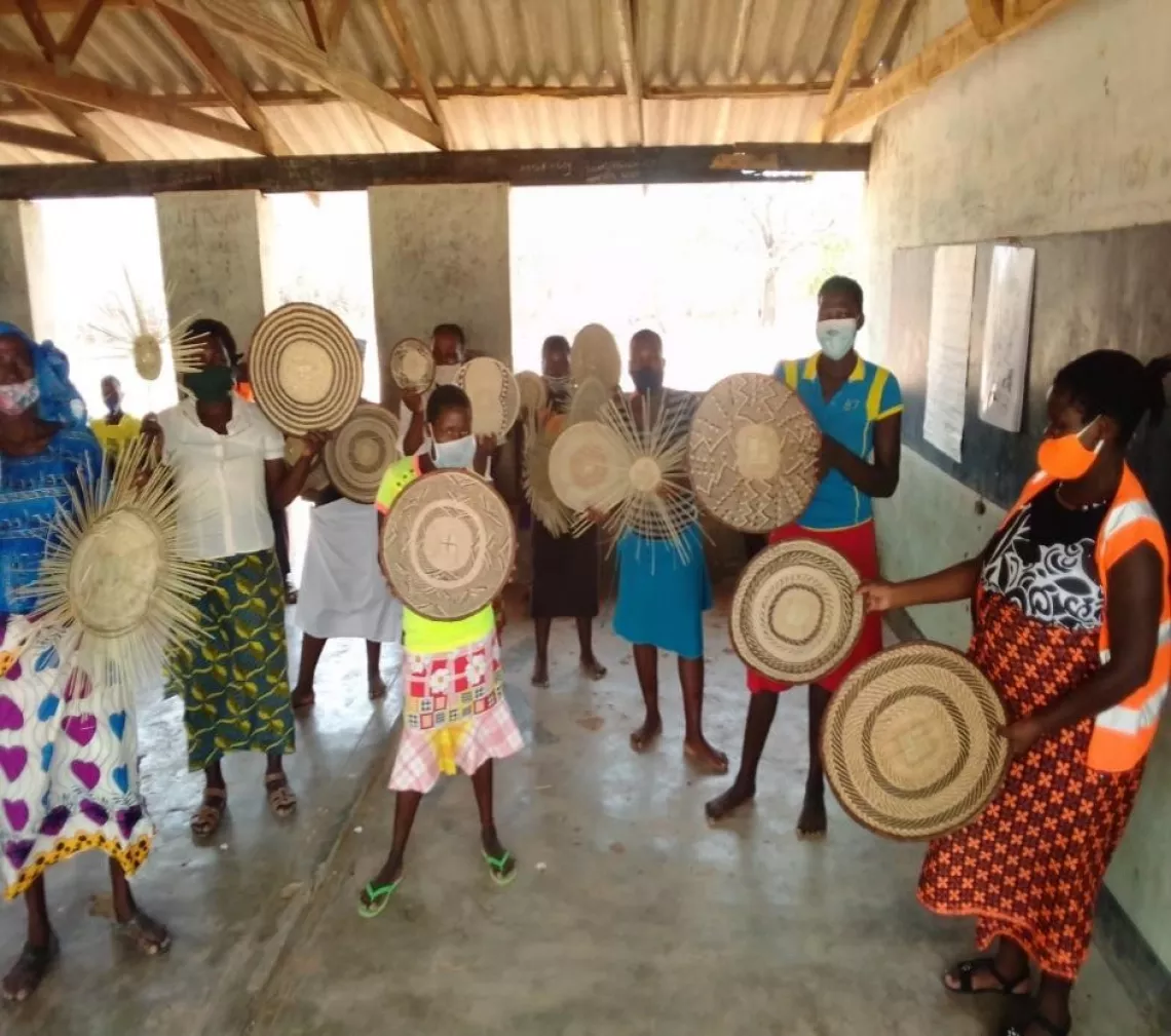 萨门德（Samende）的未成年母亲编织小组与社会心理支持官员戴安娜·穆图姆（Diana Mutumhe女士）（图右）一起展示她们制作的手工艺品，包括编好的和正在编的篮子。