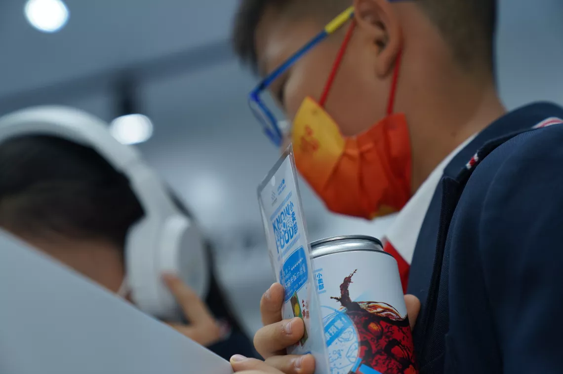 2022年5月20日，在山东省威海市科学技术馆，一名学生在参观联合国儿童基金会的知食小卖部展览时手握做成可乐罐形状的活动纪念品拼图。