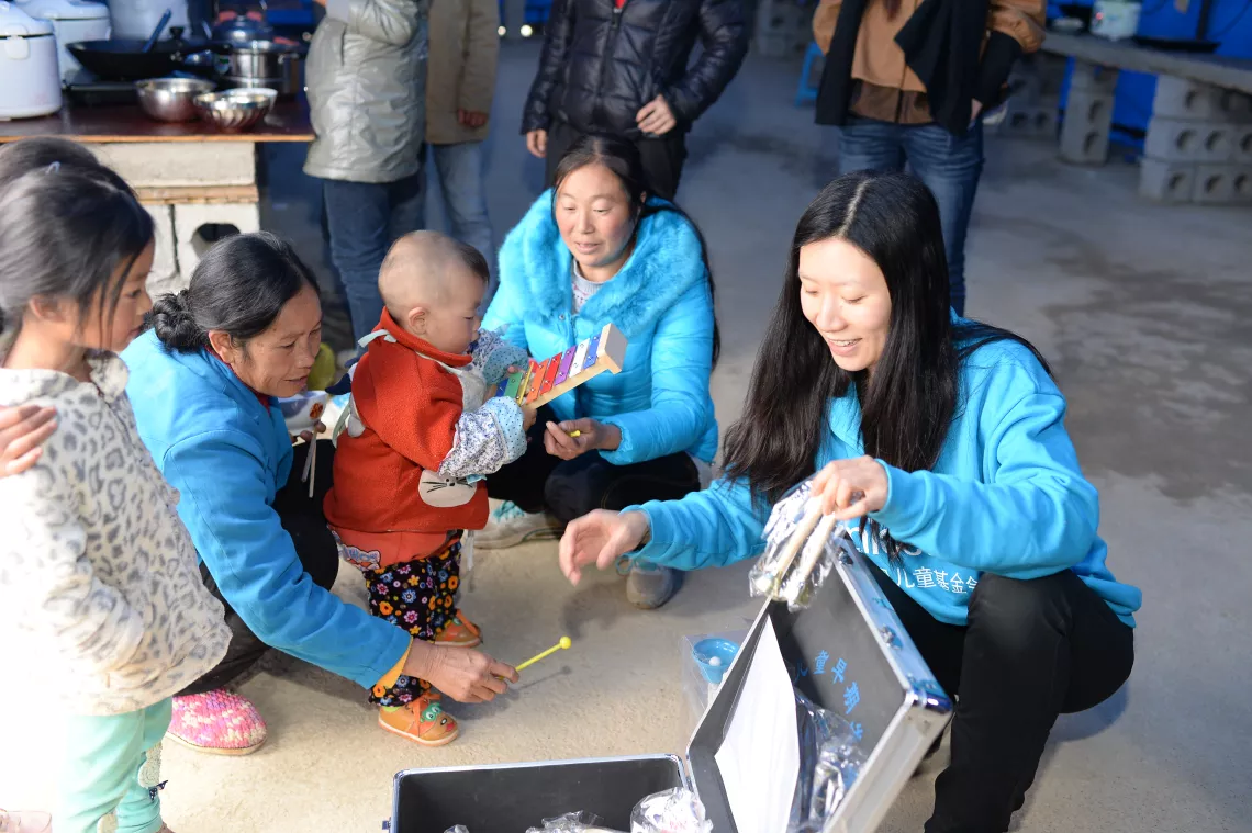 Wang Xiaolin (R1), Child Protection Officer at UNICEF China, introduces UNICEF’s Early Childhood Development kit to villagers at a shelter in Ludian, Yunnan Province, following an earthquake in 2014. 