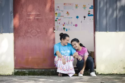 在云南盈江，儿童主任和一个女孩坐在村里的儿童之家门前。