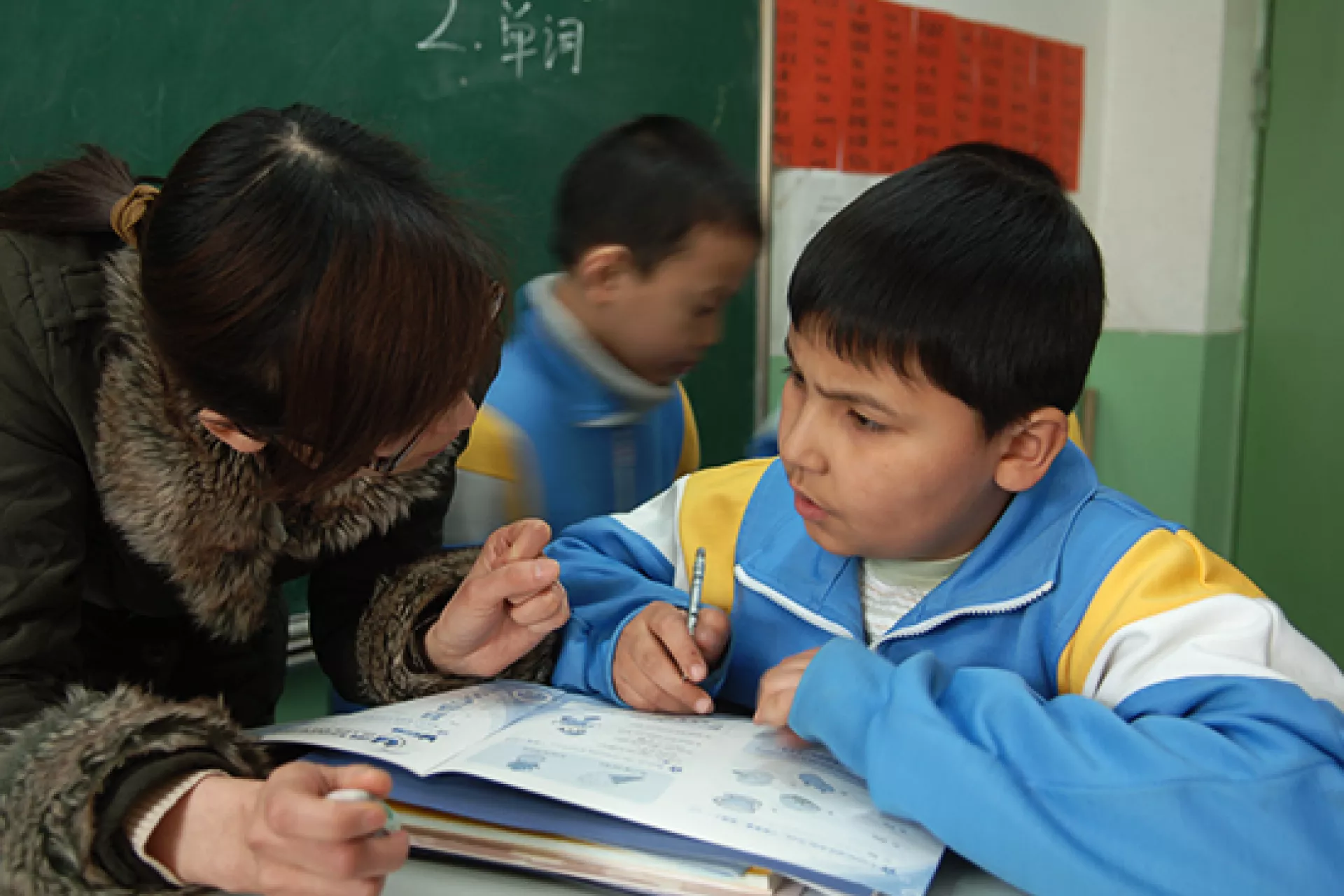 北京一所打工子女学校的老师给一名学生指导功课。