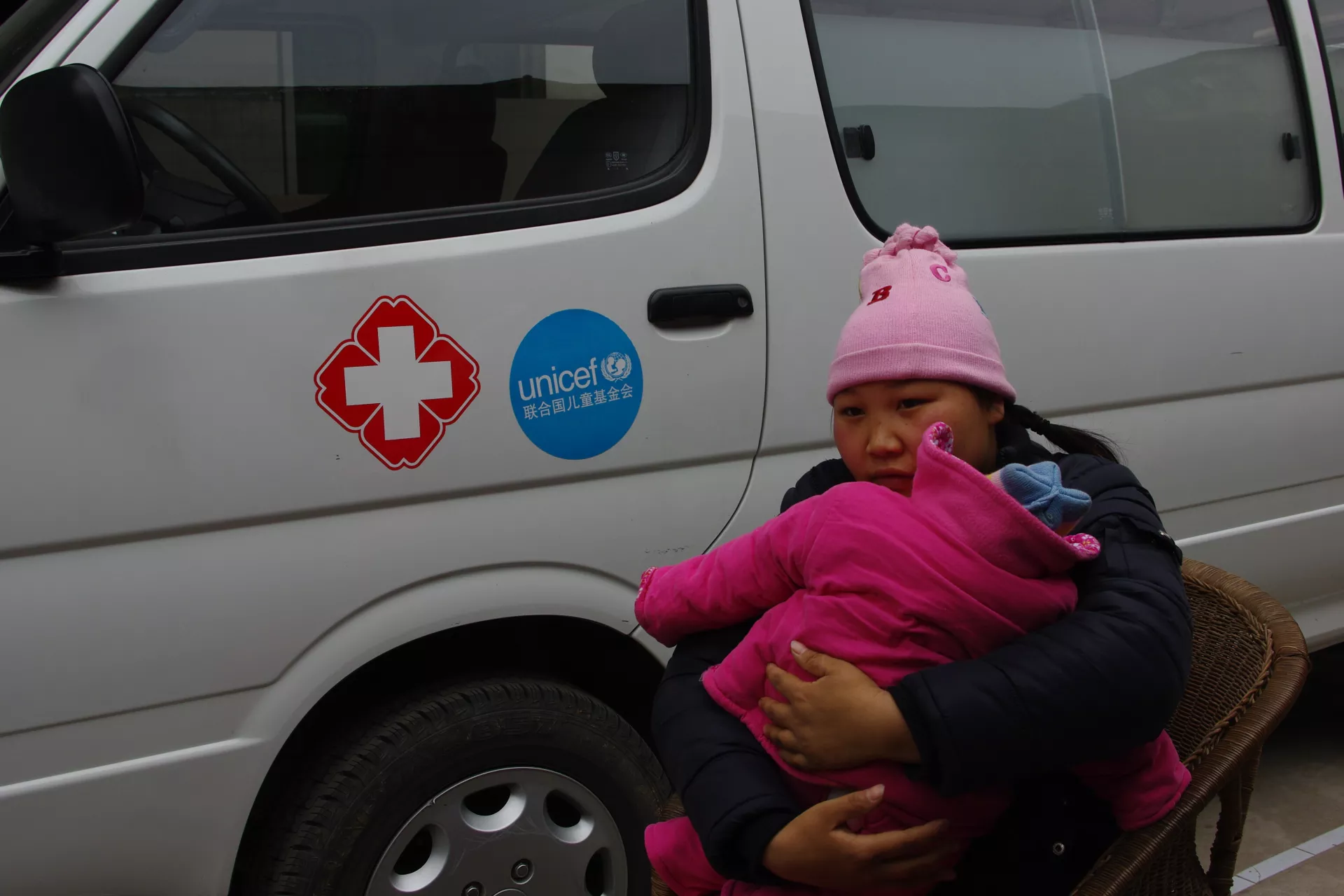 刘菊抱着女儿坐在救护车前。联合国儿童基金会为汶川地震灾区提供了大量的药品和医疗设备。
