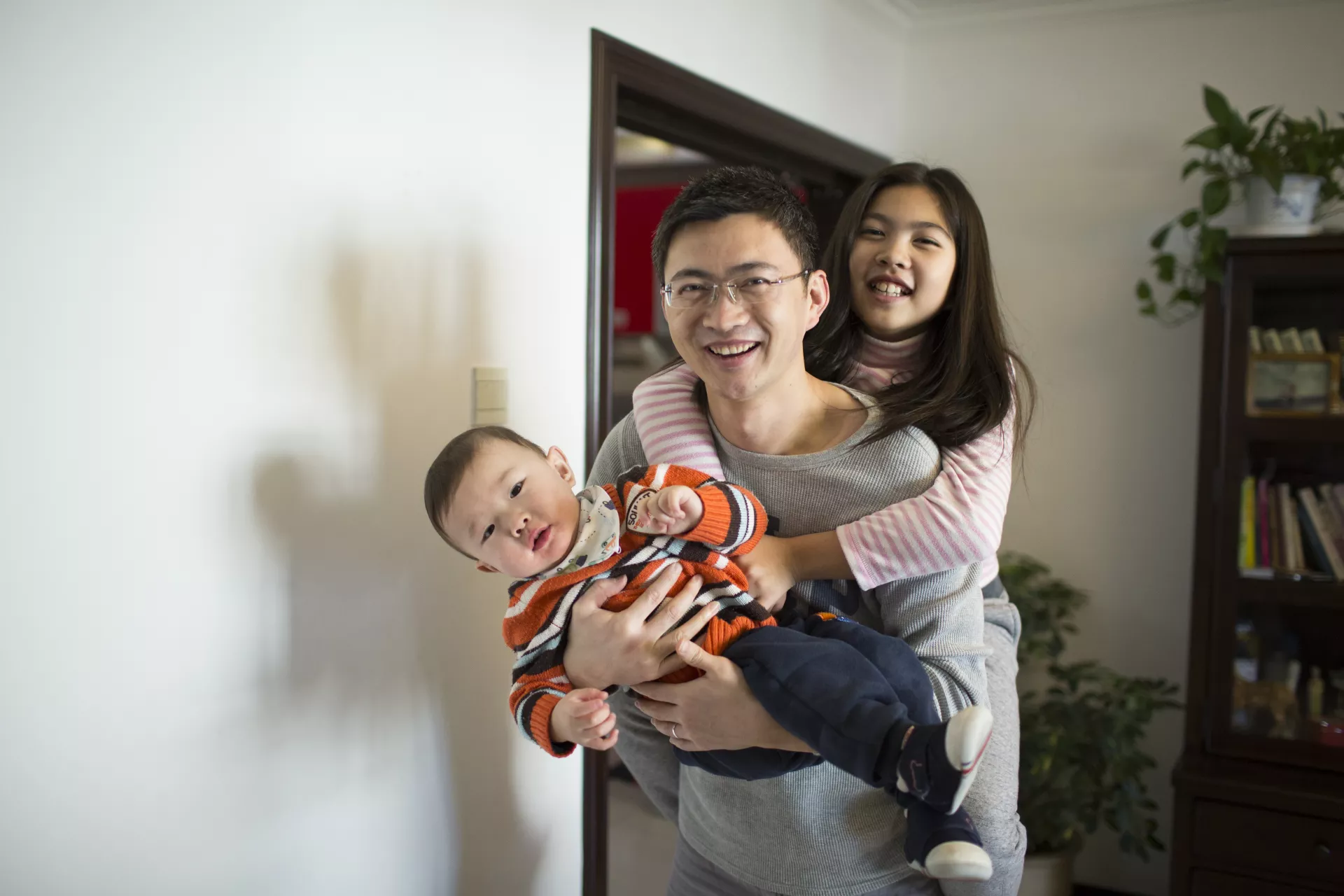 2016年，一名父亲在北京的家里背起两个孩子，与他们玩耍。