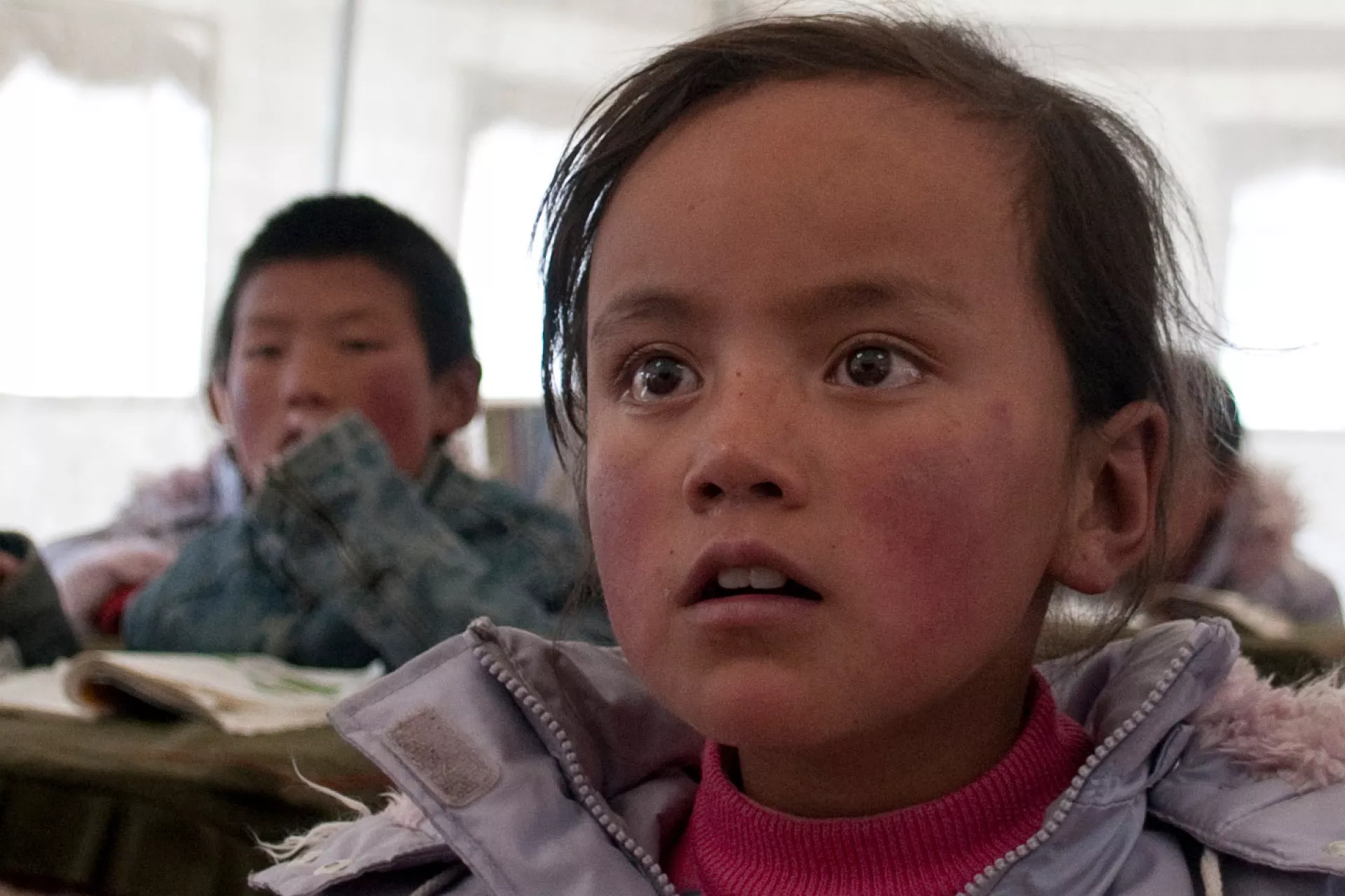 在帐篷教室内，一个女孩正在专注地听老师上课。
