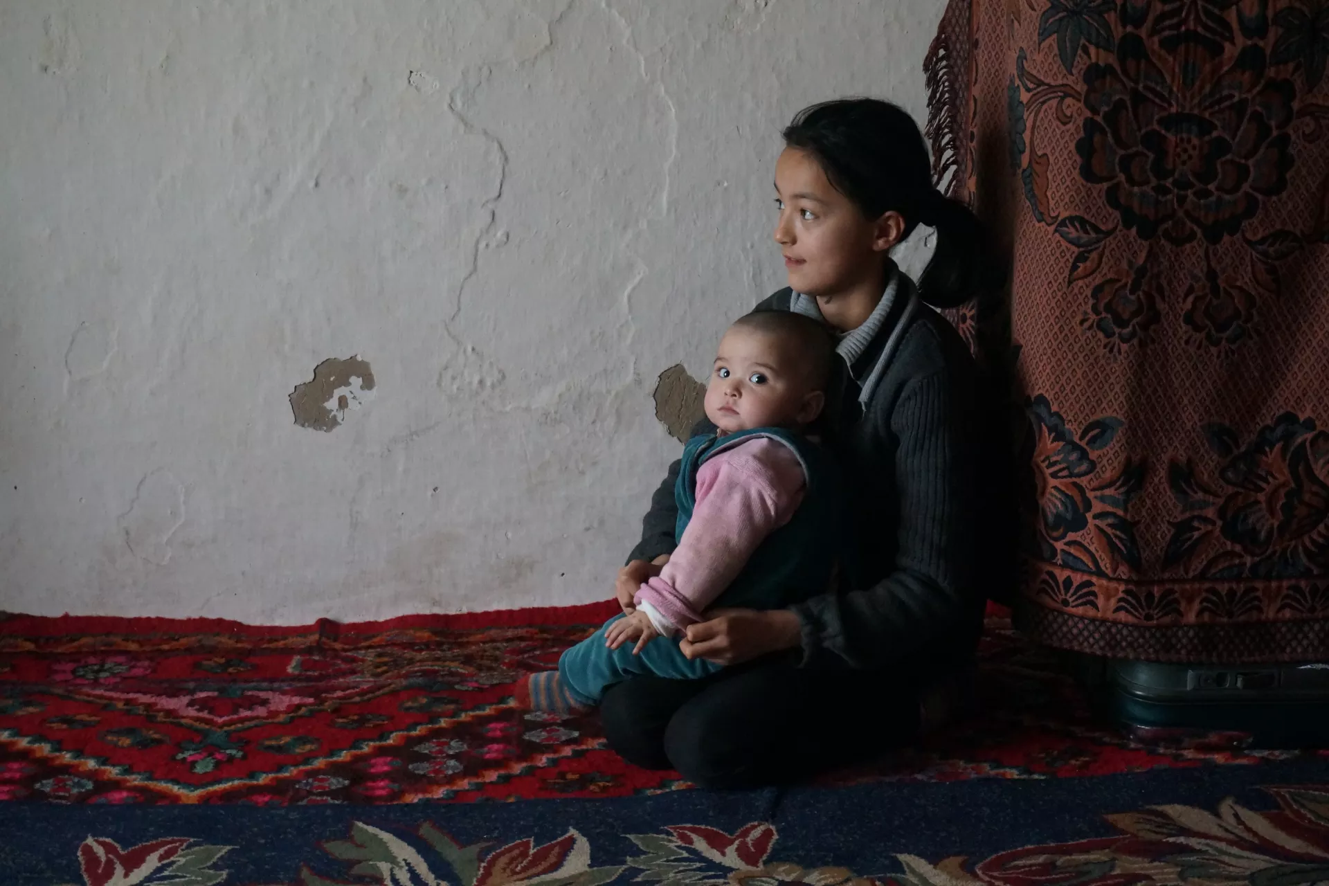 在新疆维吾尔自治区伊宁县和田买里村，一名维族女孩在家里照顾年幼的妹妹。