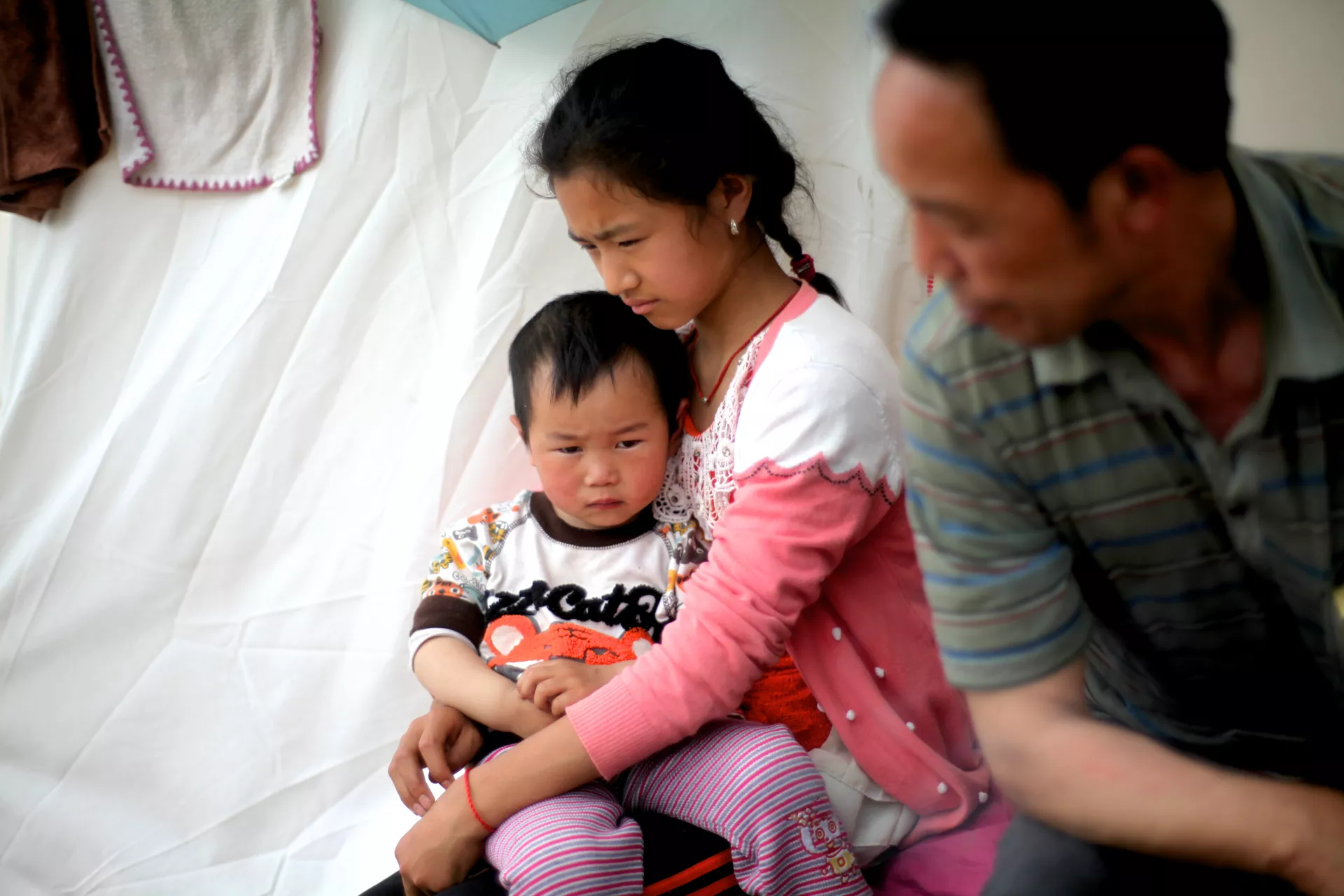 April 25, 2013, A young girl is cradling her brother in front of a tent in a temporary settlement area, Longmen Township, Sichuan Province.