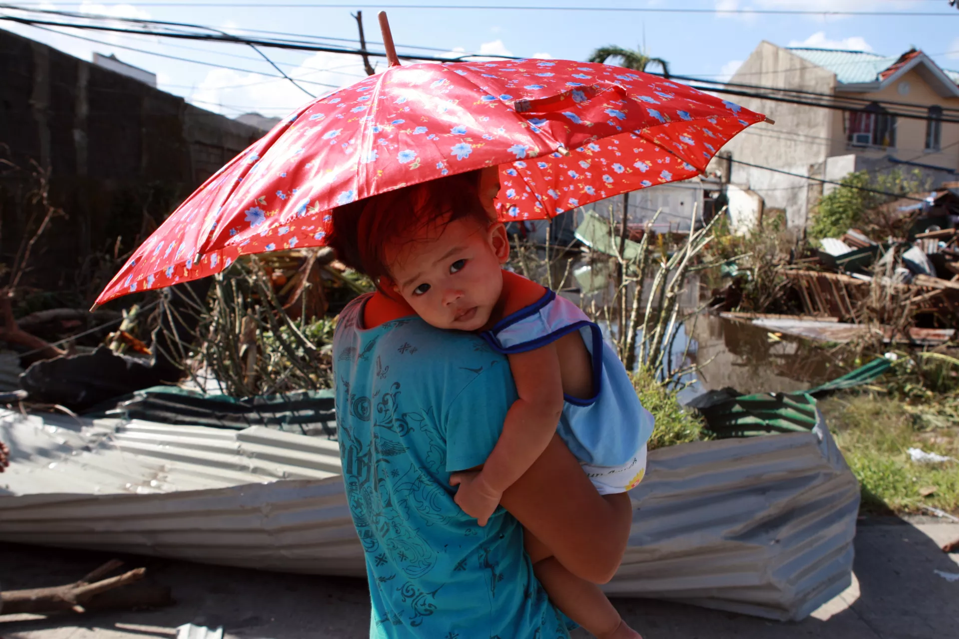 A woman carrying her daughter under an umbrella walks past some of the damage and destruction caused by Super Typhoon Haiyan, in Tacloban City.