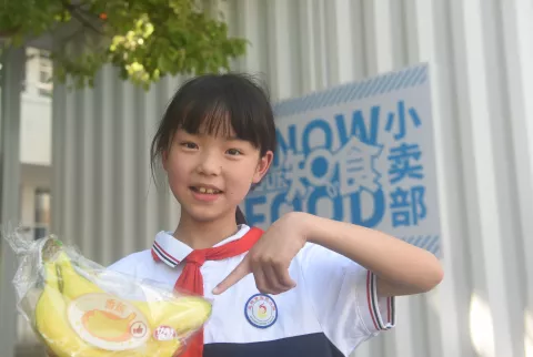 2022年5月20日，在湖北省恩施州恩施市实验小学的联合国儿童基金会知食小卖部外，一名学生展示什么是健康食物。