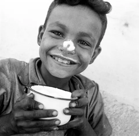 Circa 1950, approximate locale Guatemala, a smiling eight-year-old boy has milk on his nose and upper lip after drinking from his cup of UNICEF-supplied milk.