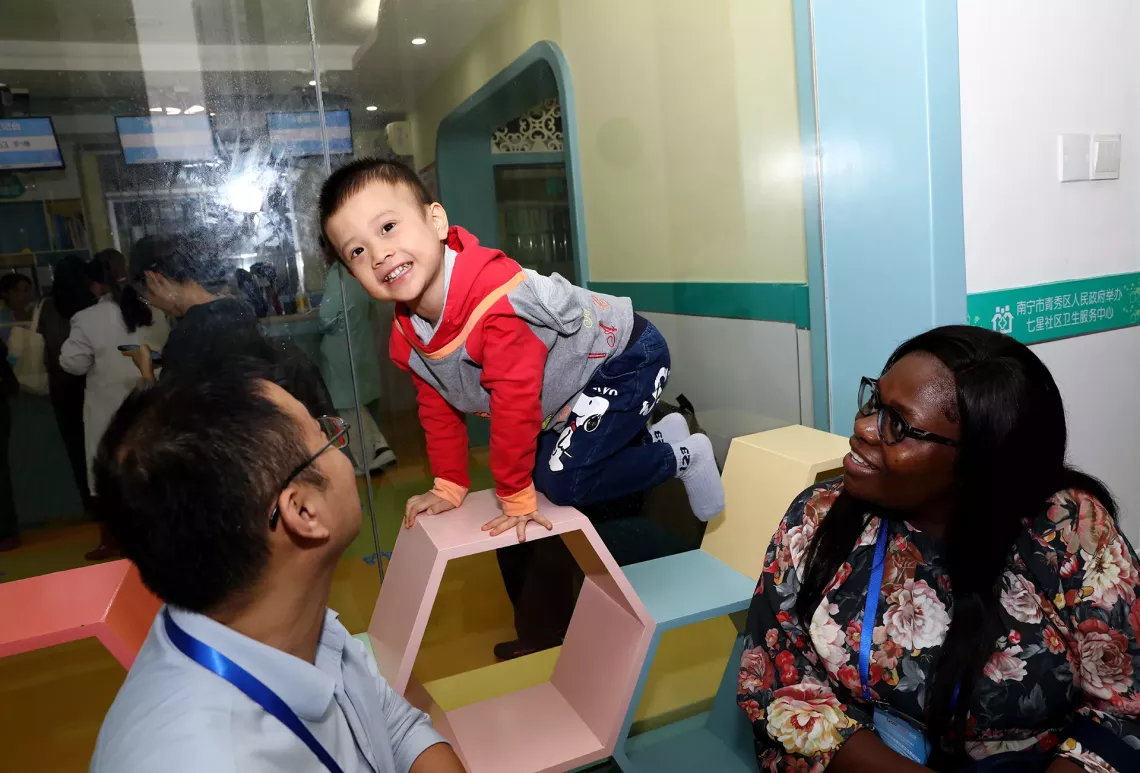 2023年11月24日，四岁的梁裕铭在七星社区卫生服务中心接受了疫苗接种和其他儿童保健服务后，与来自津巴布韦的代表（右）和联合国儿童基金会驻华办事处工作人员（左）一同玩耍。