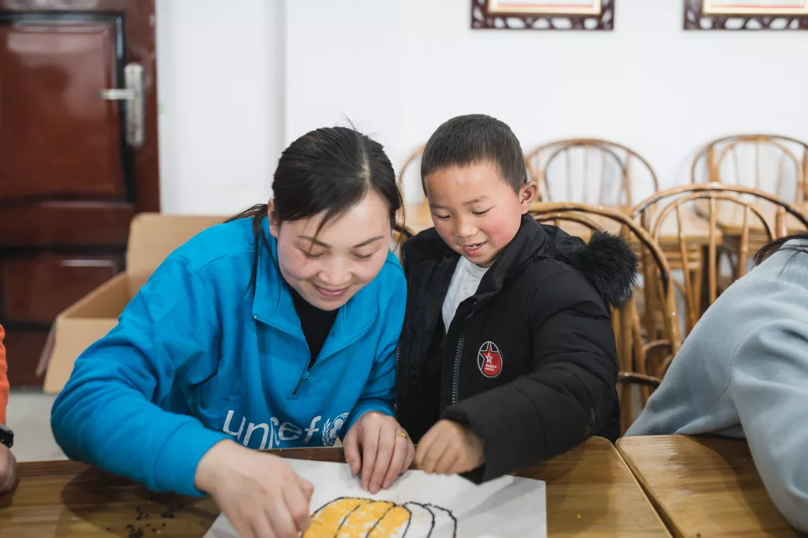 Xiaohua and a Child-Friendly Space staff member use sesame and millet to paint a pumpkin.