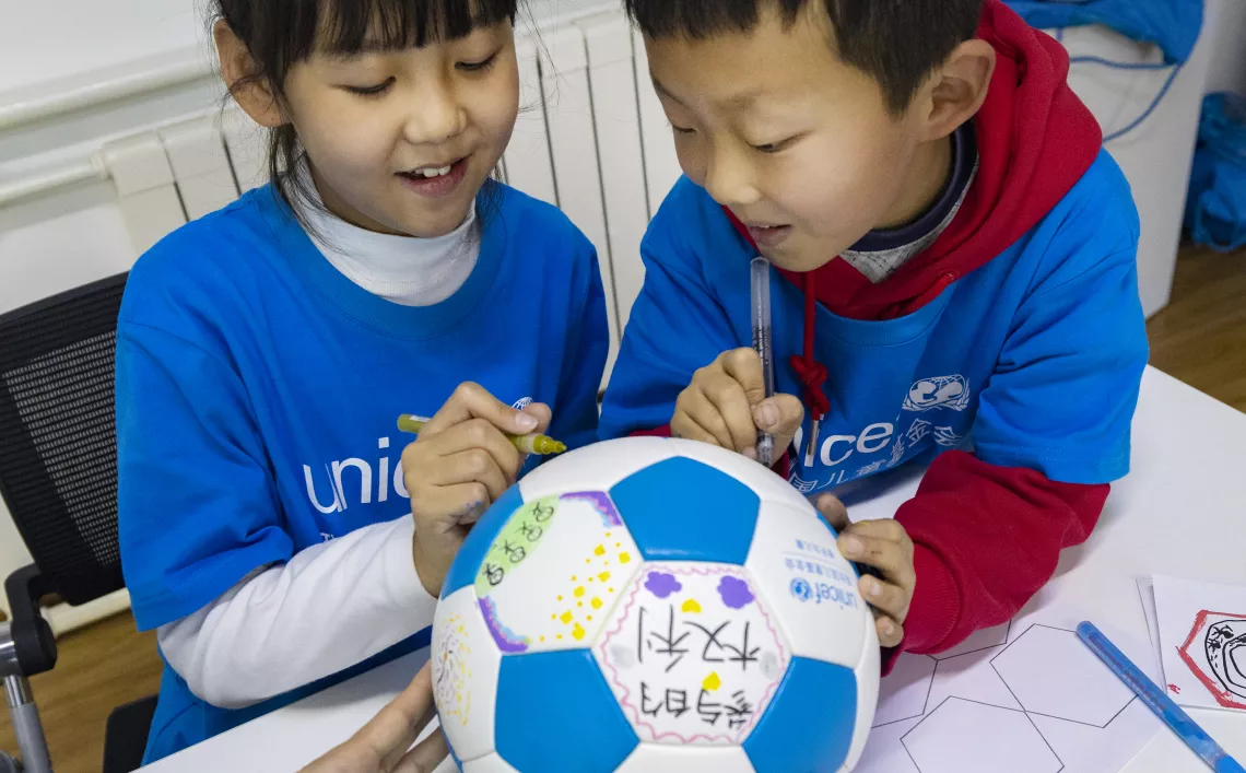 A girl and a boy draw on a football to express their perspectives on child rights ahead of World Children's Day at UNICEF China's office in Beijing on 5 November 2022. UNICEF hosted a workshop for children aged 8-14 years to express their perspectives on their right to survival, development, protection, participation, inclusion, and non-discrimination.