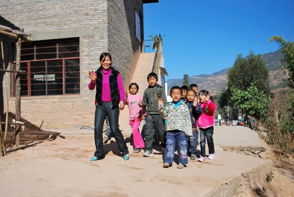 Ms. Xiong Jianying and students at the entrance of the Shuidi Teaching Site, situated at a mountain top in Yongping County, Yunnan Province.