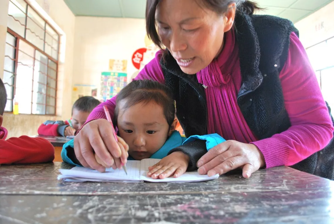 Xiong holds the hand of Nana, aged four, to show her how to write.