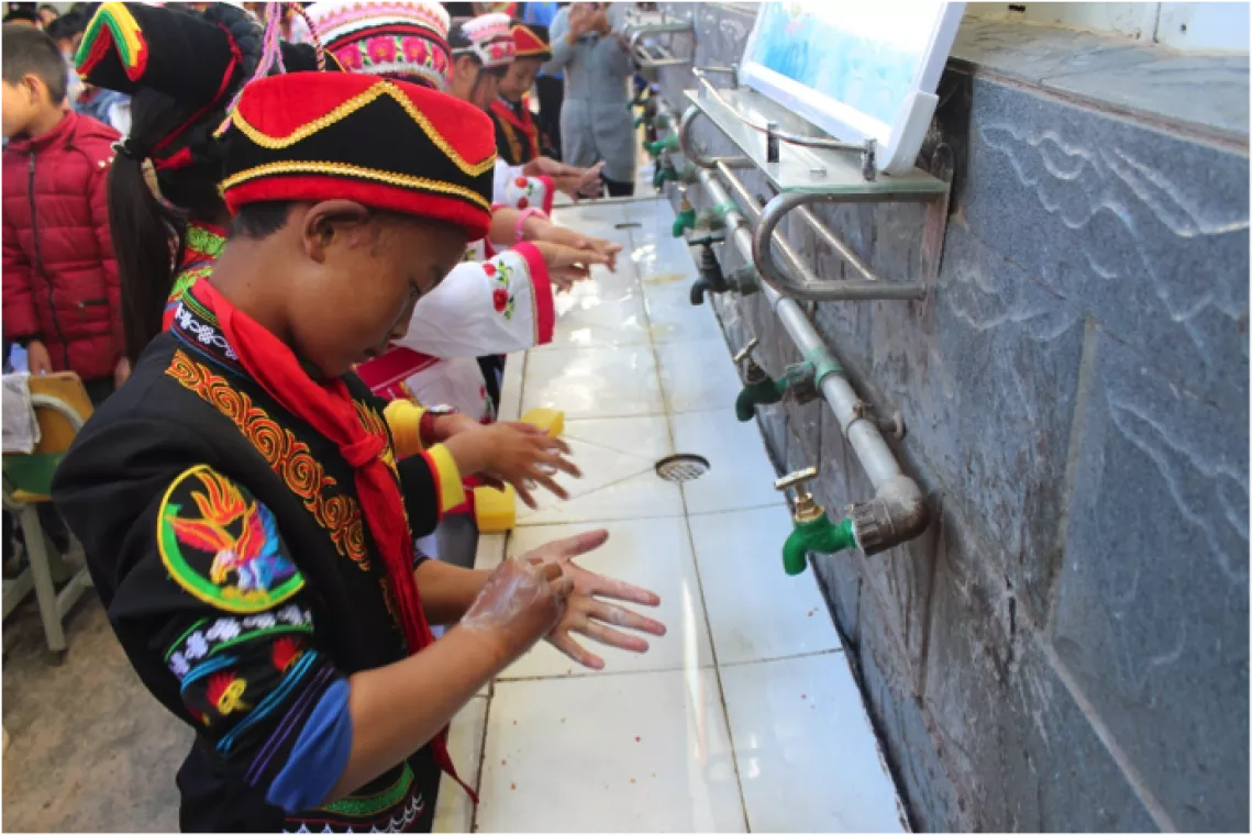Students in traditional clothes practice six-step handwashing