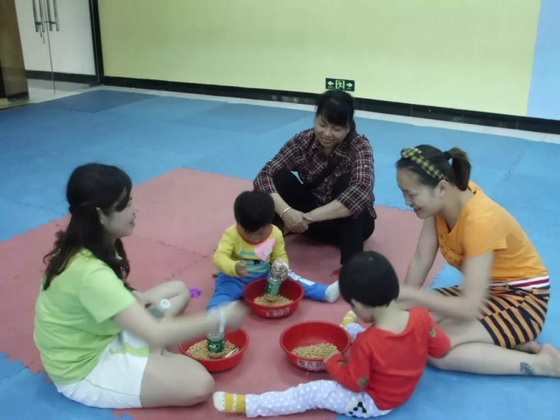 A volunteer teaches parents how to use household materials to stimulate children's motor development.