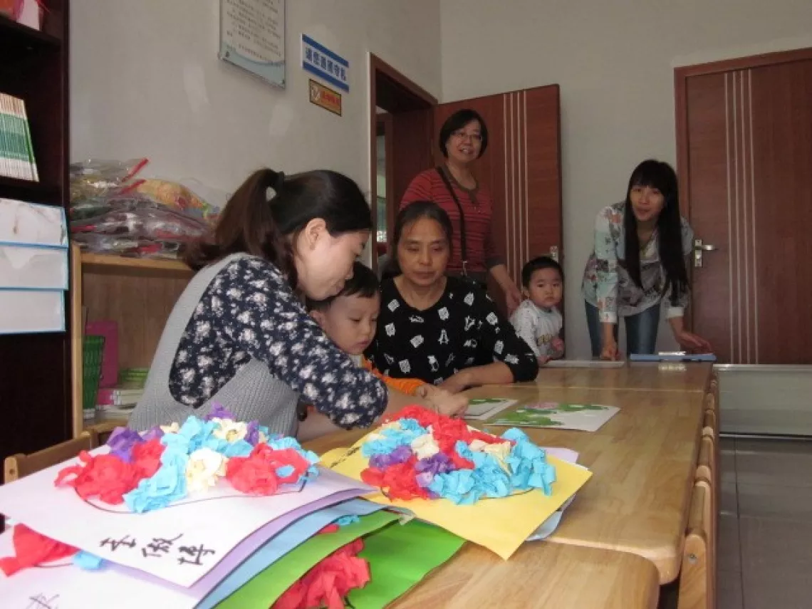 A child, her grandparent and a volunteer make game pieces together in a community centre in Hunan Province.