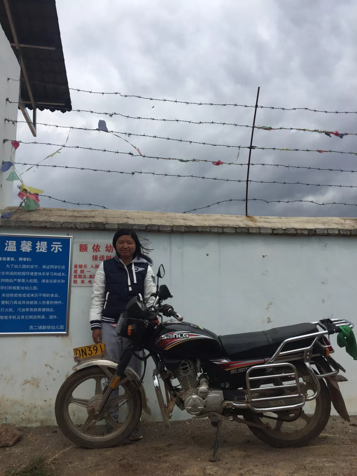 Fang Fang, principal of Eyi Kindergarten in Yunnan Province, stands behind her motorcycle outside the kindergarten.