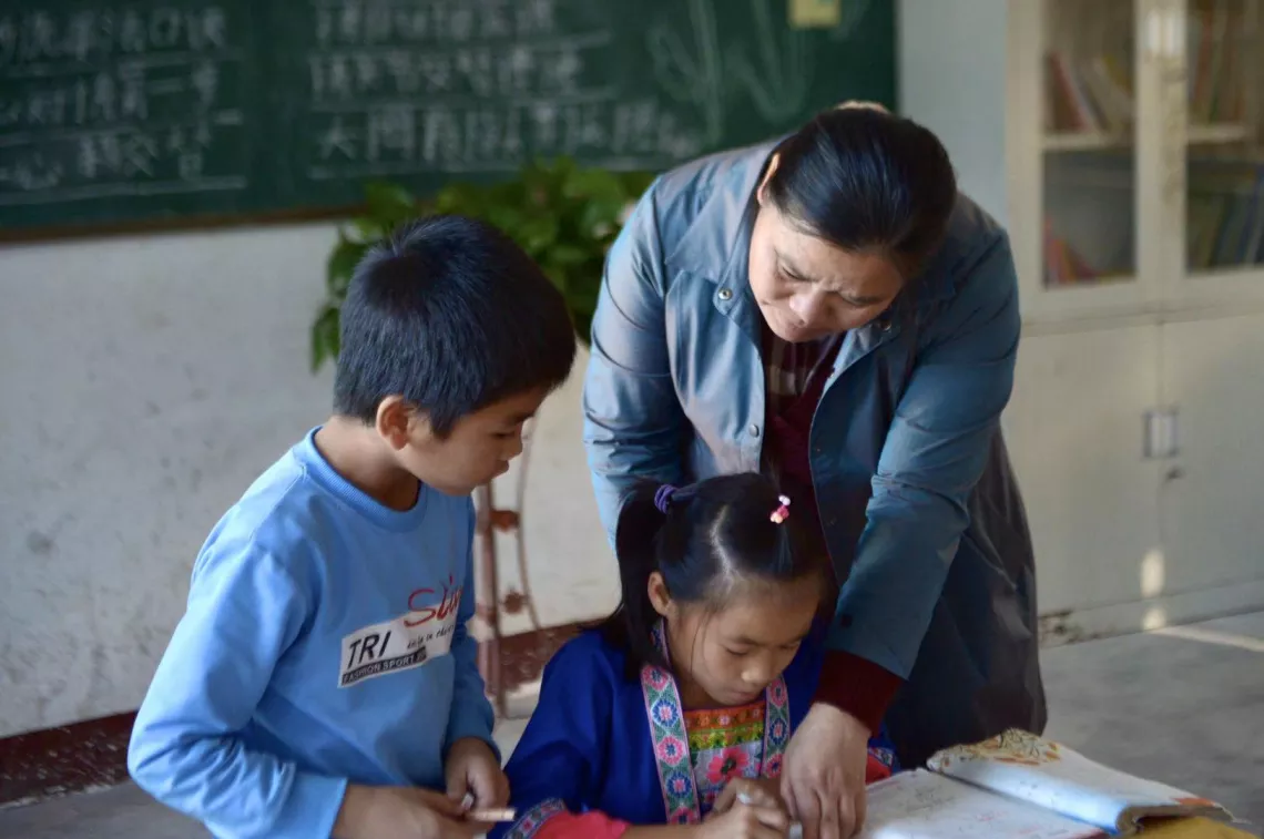 广西三江侗族自治县八江镇岩脚小学教师（右一）在给学生辅导功课。