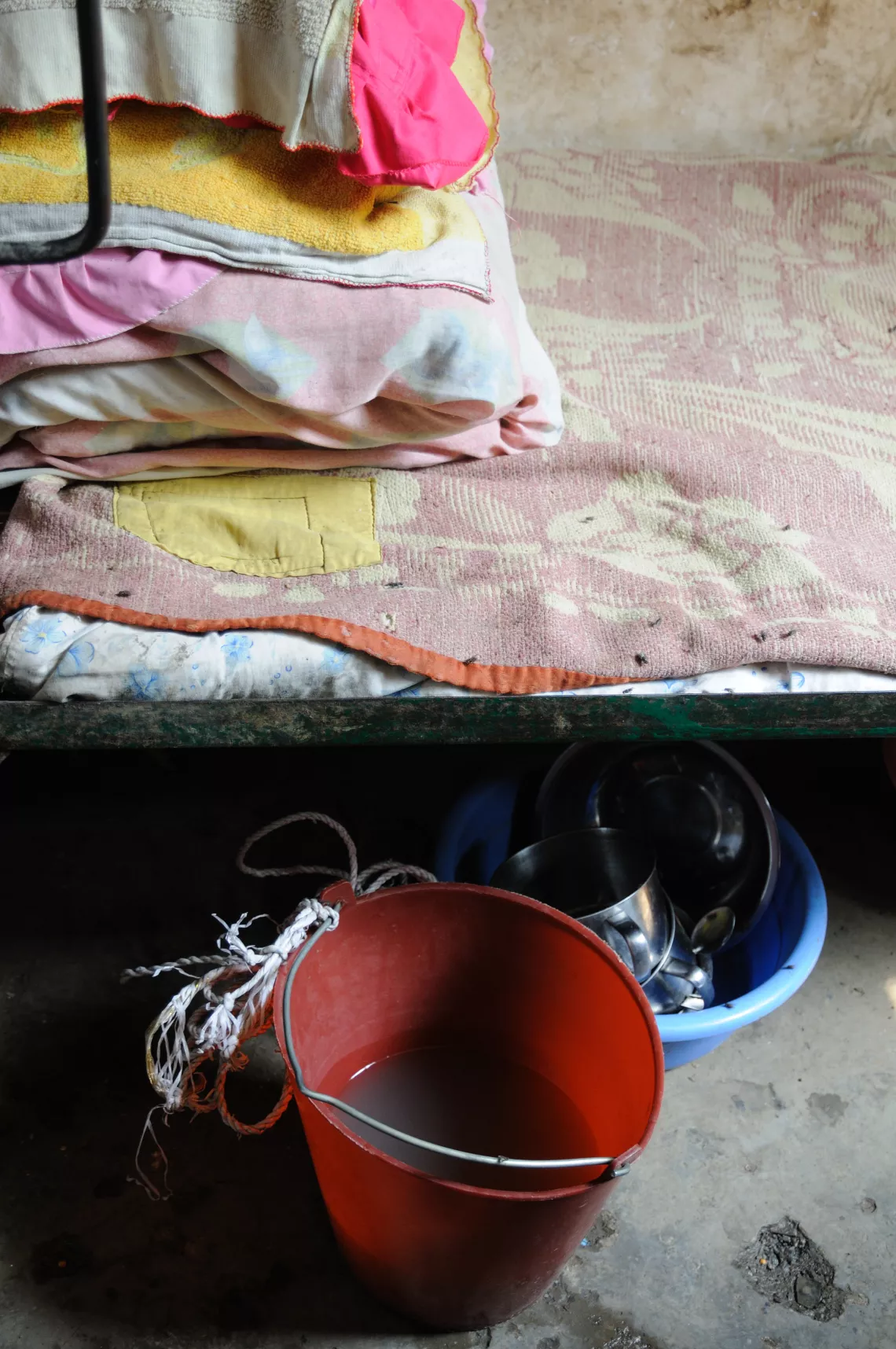 Flies crawl on the bed sheets, a water bucket and food containers in a dormitry room at Baotai Primary School.