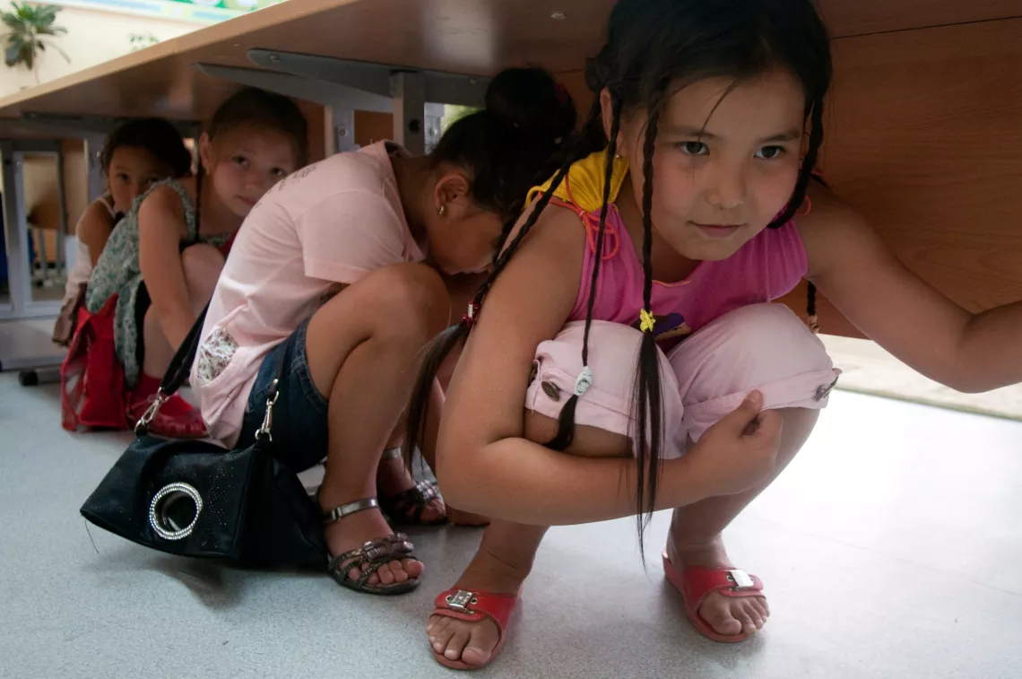 在哈萨克斯坦，四年级的学生们正躲在桌子下面，做地震时的救生模拟练习。