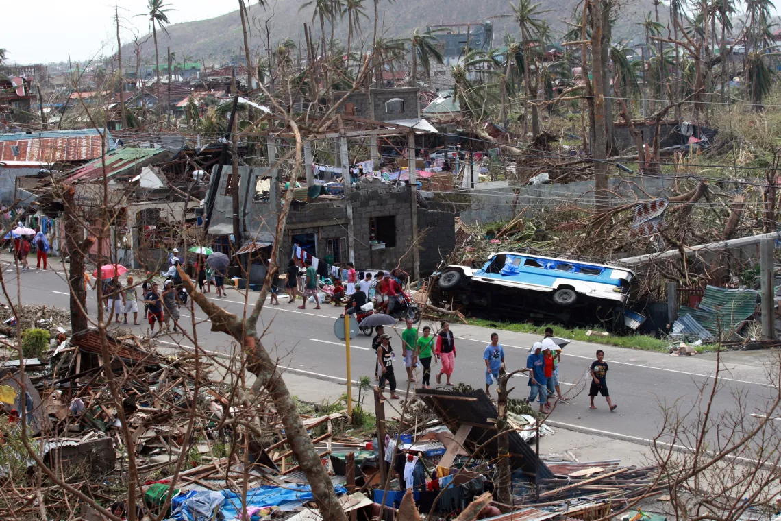 Residents walk past downed trees and destroyed homes and cars, on a road in Tacloban City.