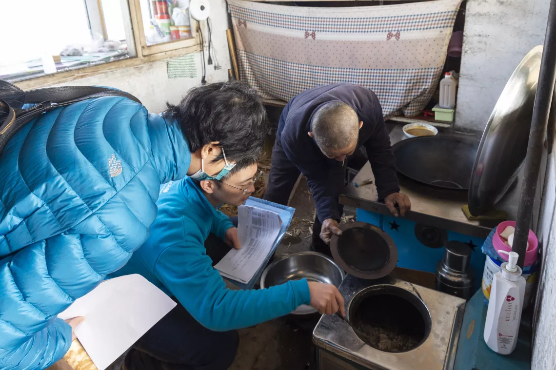 Sun Hui (middle), a programme officer from UNICEF China, checks the traditional stove during a visit to a rural household in Jiamusi, Heilongjiang Province, on 30 November 2020.