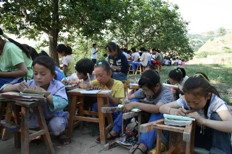 Students sit on the ground and use their stools as school desks during classes under trees in the afternoon at Qinglian School, Guochuan Village, Qingshui County, Gansu Province.