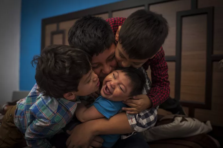 9个月大的Danilo在危地马拉的家中，他在哥哥们亲吻他的时候露出了笑容。Danilo患有先天性寨卡综合征和头小畸型，他从家庭、邻里和社区获得了爱、关注、照护与支持。