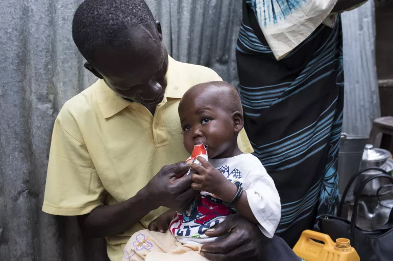 在南苏丹的首都朱巴，28岁的父亲尤萨·奥古斯蒂诺回家后给一岁7个月的孩子吉福特喂食高营养花生酱。
