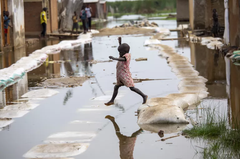 A child jumps over a puddle of water.