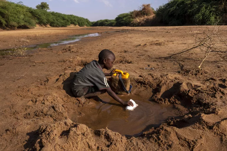 一名男孩正在尽其所能地从一条因严重干旱而干涸的河流中收集水。