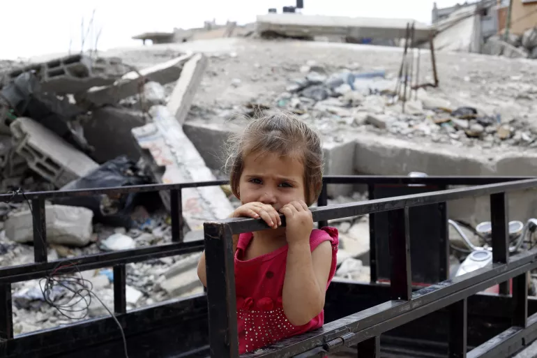 在加沙的Shejaiya社区，一名女孩站在她家被毁的屋子前。她身后的房屋废墟，现在成了孩子们游戏的操场。